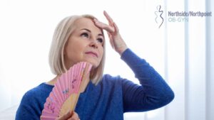 A mid-life woman fanning herself while sitting on the couch