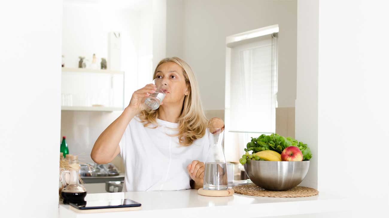 Woman in a kitchen sipping water from a glass
