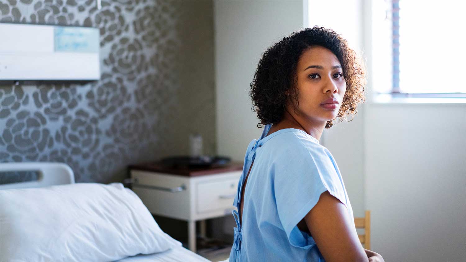 Woman sitting on a hospital bed, looking away with a thoughtful expression