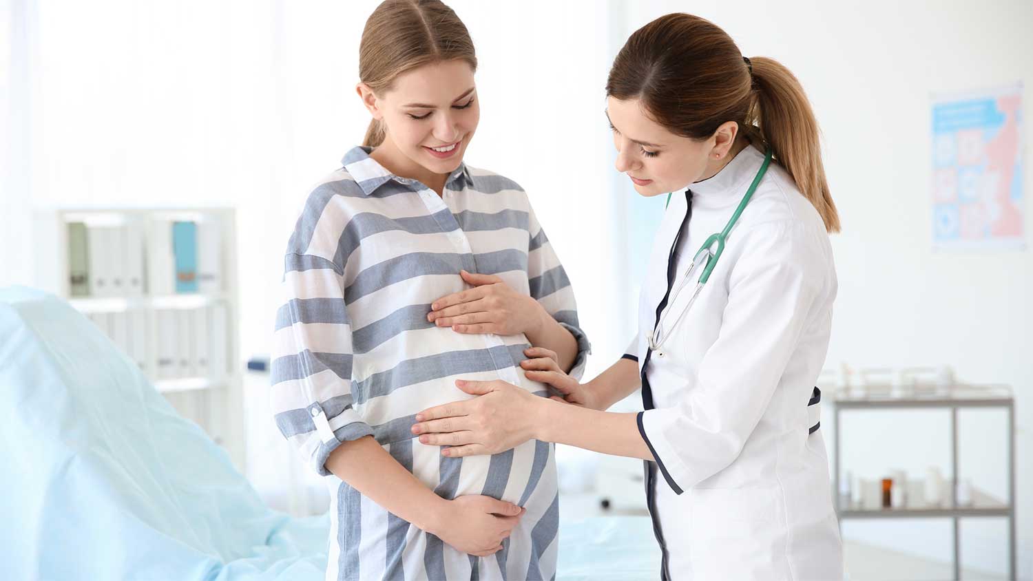  A doctor gently assessing the belly of a standing pregnant woman during a prenatal visit