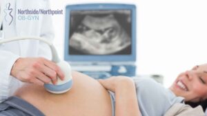 Pregnant woman lying on a bed while a medical professional performs an ultrasound in a clinic