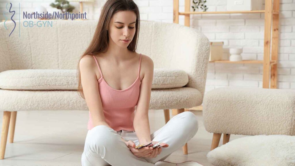 A woman sitting on the floor, thoughtfully looking at the medications in her hands.