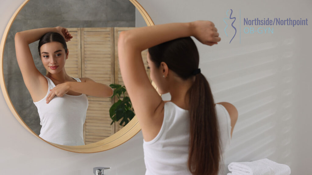 A woman standing in front of a mirror performing a self-breast exam.