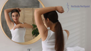 A woman standing in front of a mirror performing a self-breast exam.