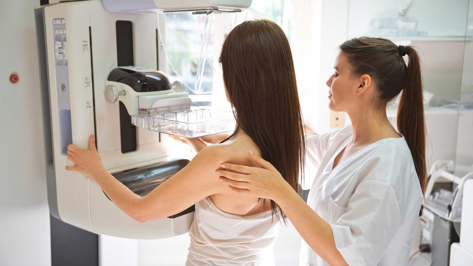 A woman receiving a mammogram from a healthcare provider.