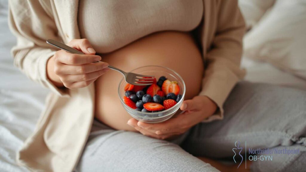 Pregnant woman eating a bowl of blueberries and strawberries.