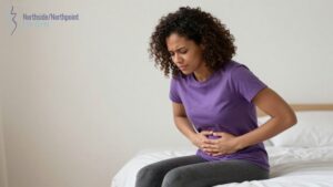 Woman sitting on bed holding lower abdomen due to pelvic pain from uterine fibroids.